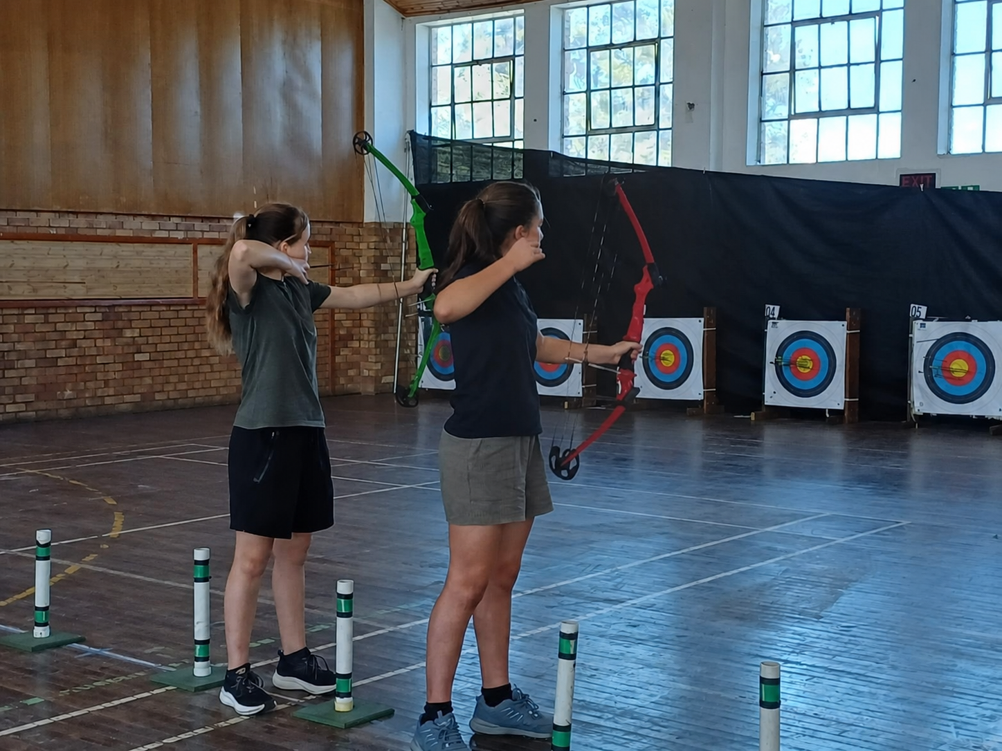 Twee CVO Omega-leerders neem deel aan binnenshuise boogskiet.